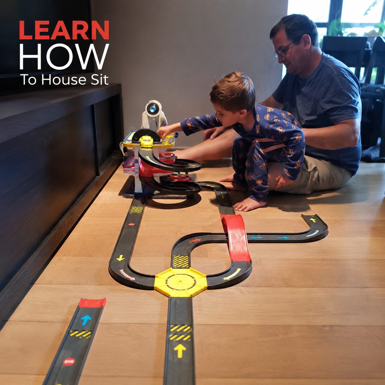 A father and son playing with a toy car track during a house sit